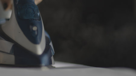 Selective focus of female hand irons white clothes with steam iron on an Ironing board. Push button of steam humidifier, laundry moistening function. Ironing linen using hot steamの写真素材