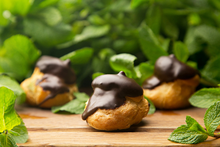 Three profiteroles with chocolate glazed with fresh mint leaves on wood boardの写真素材