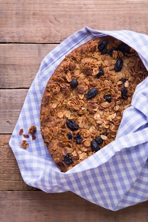 Homemade healthy banana cake with oatmeal and black raisins granola top on cotton napkin on the wood backgroundの写真素材