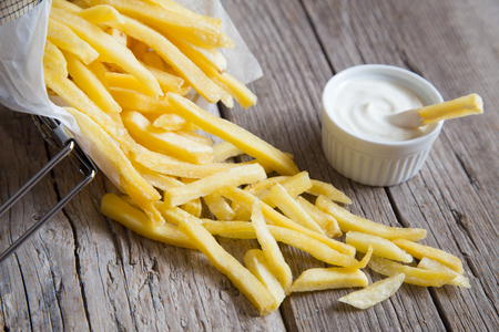 French fries in metal basket with mayonnaise on wood tableの写真素材