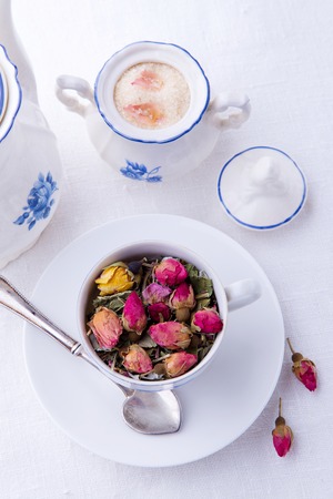 Cup of pink roses tea and sugar bowl with brown sugar and rose petalsの写真素材