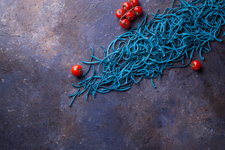 Blue Colored Pasta with cherry tomatoes on Dark Background. Flat Lay. Copy space. Top view.