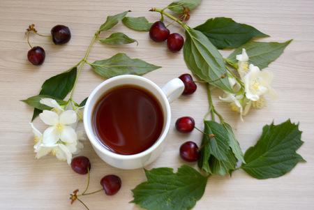 Cup of tea, cherry and flowers on the tableの写真素材