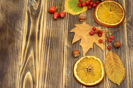 Autumn composition of colorful leaves red berries, dried oranges and nuts on a wooden background with autumn conceptの写真素材