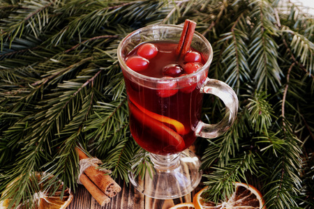Christmas mulled wine with cranberries in glass. Winter warming drink with spices. Decorated fir branches, cinnamon, dried orangesの写真素材