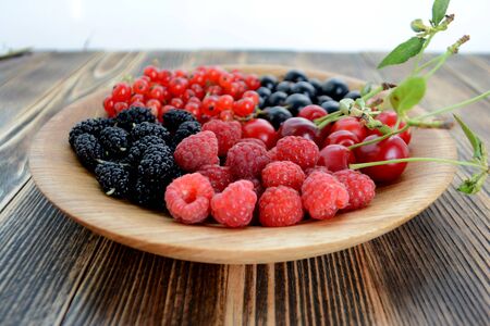 Different delicious fresh summer berries cherry, currant, blackberry in wooden plate on wooden backgroundの写真素材