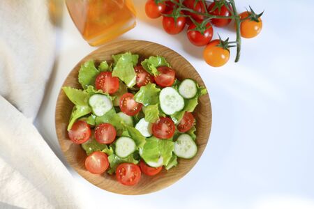 Spring or summer salad with fresh vegetables, cherry tomatoes and cucumbers in a wooden plate on whiteの写真素材