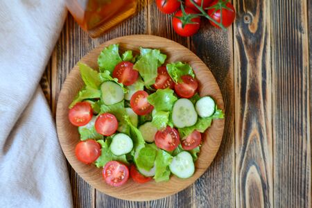 Spring or summer salad with fresh vegetables, cherry tomatoes and cucumbers in a wooden plate on   woodenの写真素材