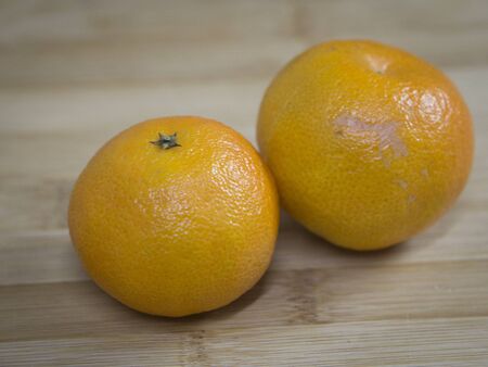 two whole tangerines lie on a wooden surfaceの写真素材