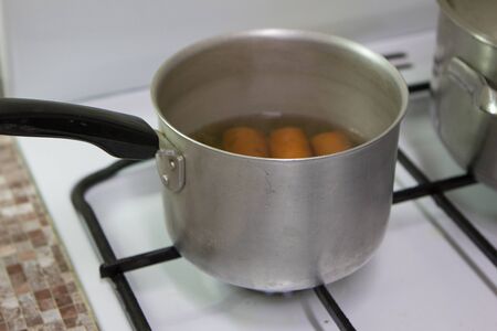 The pan is on the gas stove with carrots insideの写真素材