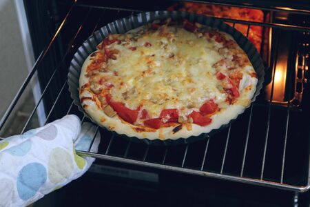 A hand in the kitchen grab pulls a cooked pizza out of the ovenの写真素材