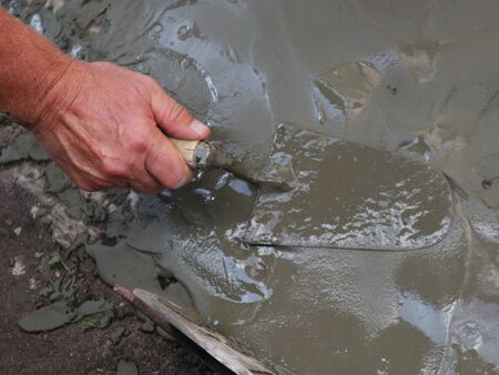 a man's hand works with a spatula leveling the cement layerの写真素材