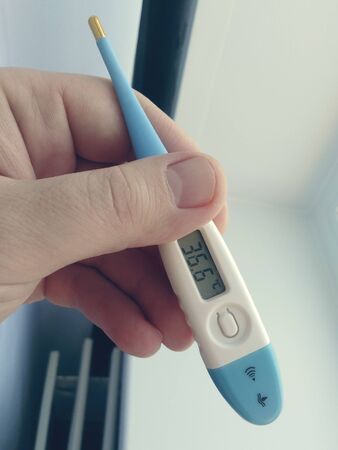 A man's hand holds a thermometer with a normal temperature readingの写真素材