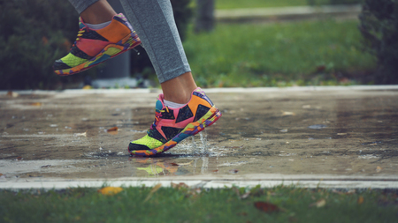 Young woman running on asphalt sports field in rainy weather splashing puddles.の写真素材