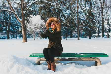 Young woman playing with snow in the park sitting on the benchの写真素材