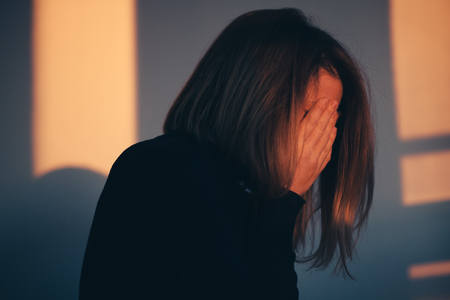 A woman sitting alone and depressed in window lightの写真素材