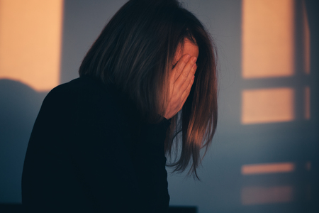 A woman sitting alone and depressed in window lightの写真素材