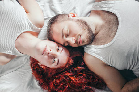 Top view of a happy couple heads to each other on white bed sheetsの写真素材