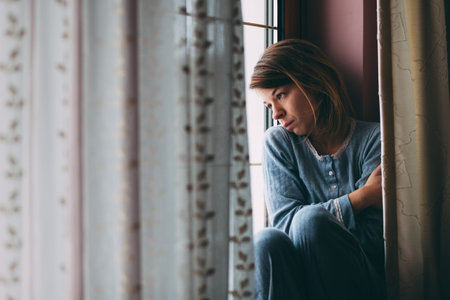 Young sad woman sitting on the window looking outside