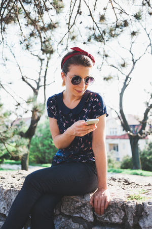 Young woman sitting in the park using smartphoneの写真素材