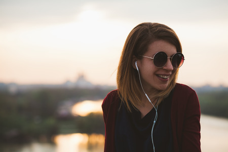 Young woman enjoying sunset listening to the music on the smartphoneの写真素材