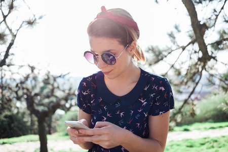 Young woman sitting in the park using smartphoneの写真素材