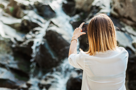 Young woman taking a photo of the waterfall in natureの写真素材