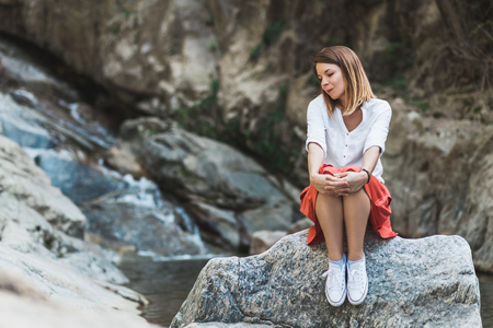 Young woman sitting on the rock by the river thinkingの写真素材