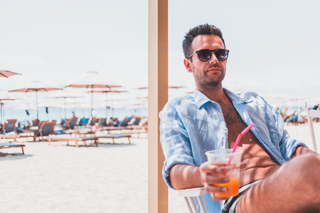 Young man drinking fresh orange juice in the beach barの写真素材