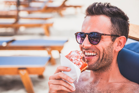 Young handsome man eating doughnut on the beachの写真素材