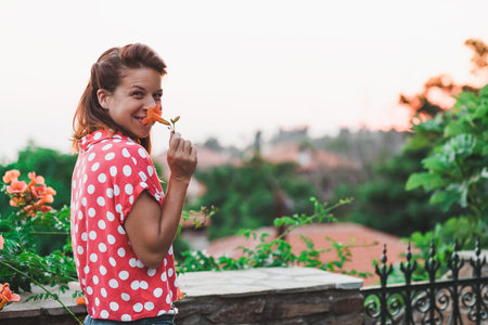 Young woman smelling flower in the garden enjoying sunsetの写真素材