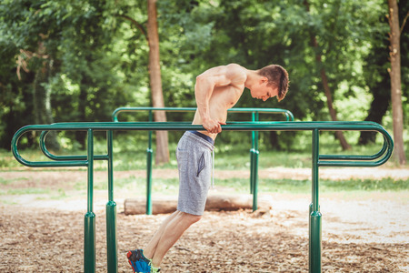Young fit man doing push ups on bars in an outdoors gymの写真素材
