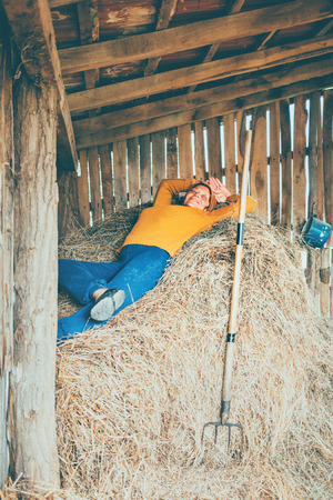 A mature woman taking a break while working on a farm, laying down in a strawの写真素材