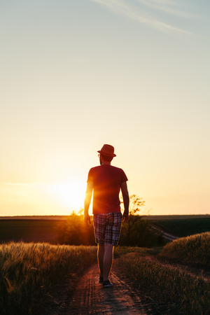 Young man walking on the muddy road into the sunsetの写真素材