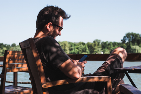 Young man in a cafe by the river using smartphoneの写真素材