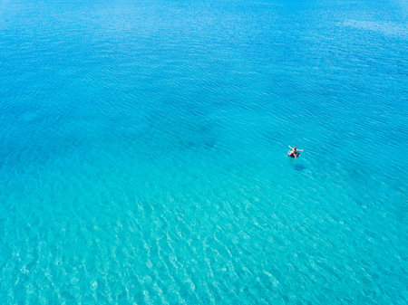 Aerial view of woman floating on the water mattress in the turquoise sea