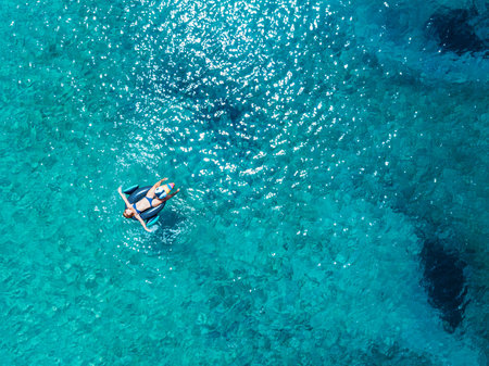 Aerial view of woman floating on the water mattress in the turquoise sea