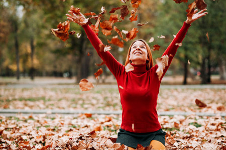 Young woman throwing autumn leaves in the air in the park