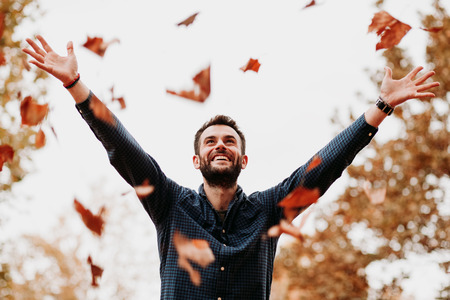 Young man throwing autumn leaves in the airの写真素材