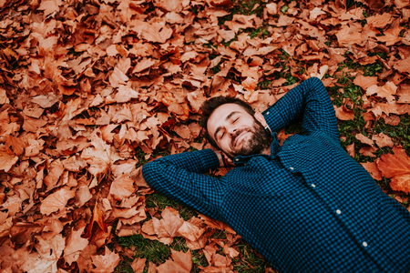 Young man lying down on the ground covered in autumn leavesの写真素材