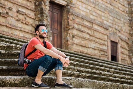 Young male traveler sitting on steps in old town in Tuscany, Italyの写真素材