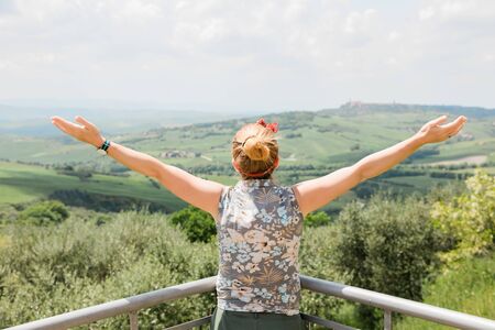 Young woman standing with her arms stretched enjoying the view of the Tuscany landscapeの写真素材