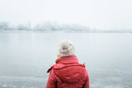 Back view of a woman looking at a frozen lake in winter morning