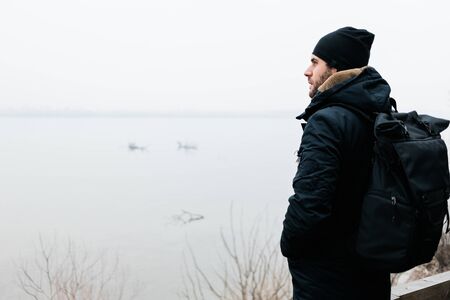 Young man standing by the river in winter morningの写真素材