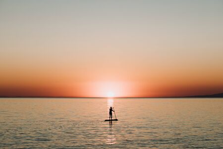 Woman paddling on a board on the sea in sunsetの写真素材