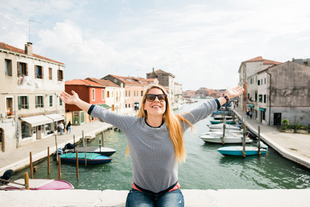 Young female traveler sitting on a bridge with her arms stretched in Murano in Venice, Italyの写真素材
