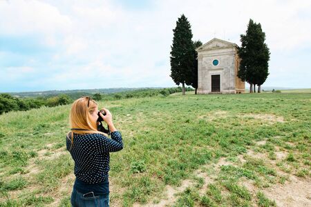 Young female traveler taking a photo of a famous church in fields of Tuscany, Italyの写真素材
