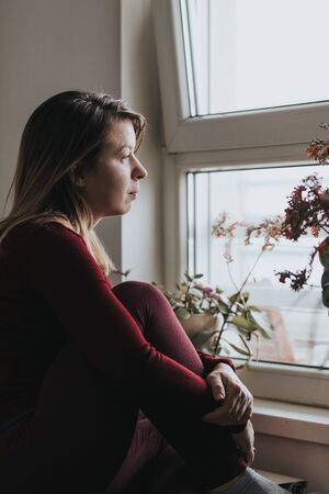 Young worried woman looking through the windowの写真素材