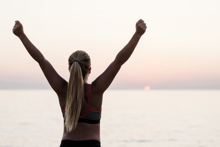Young woman standing by the sea with arms raised in triumphの写真素材