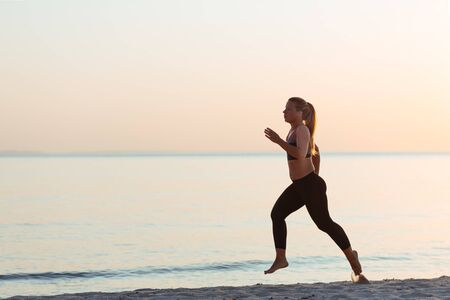 Young sporty woman running on the beachの写真素材